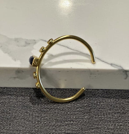 Side view of Handmade Gold-plated bangle with blue lapis lazuli gemstone on a marble surface