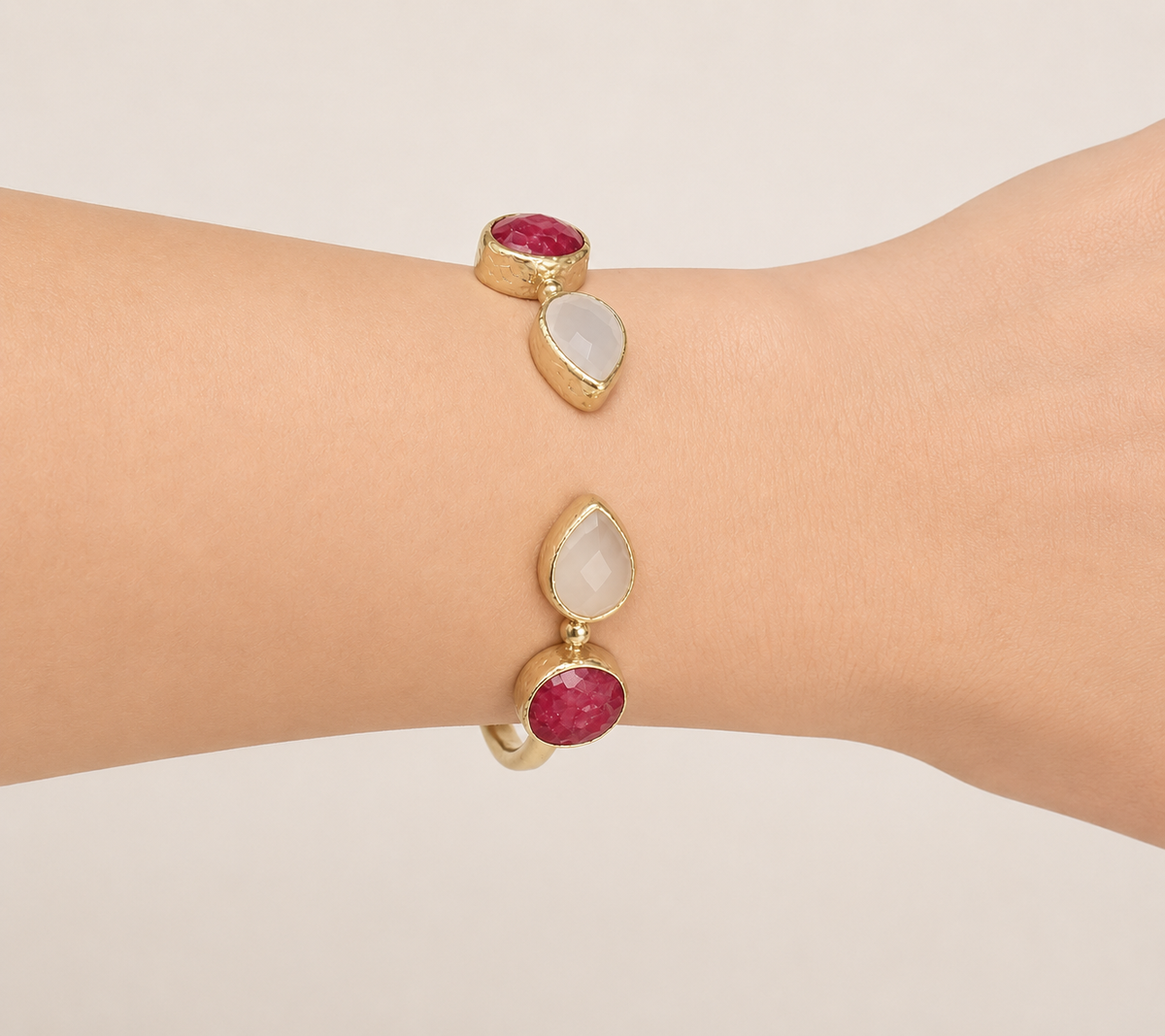 A close-up side view of a person's wrist wearing m gold-plated snow Quartz and Ruby adjustable cuff bracelet.