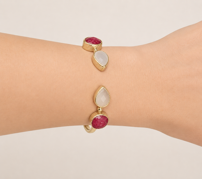 A close-up side view of a person's wrist wearing m gold-plated snow Quartz and Ruby adjustable cuff bracelet.
