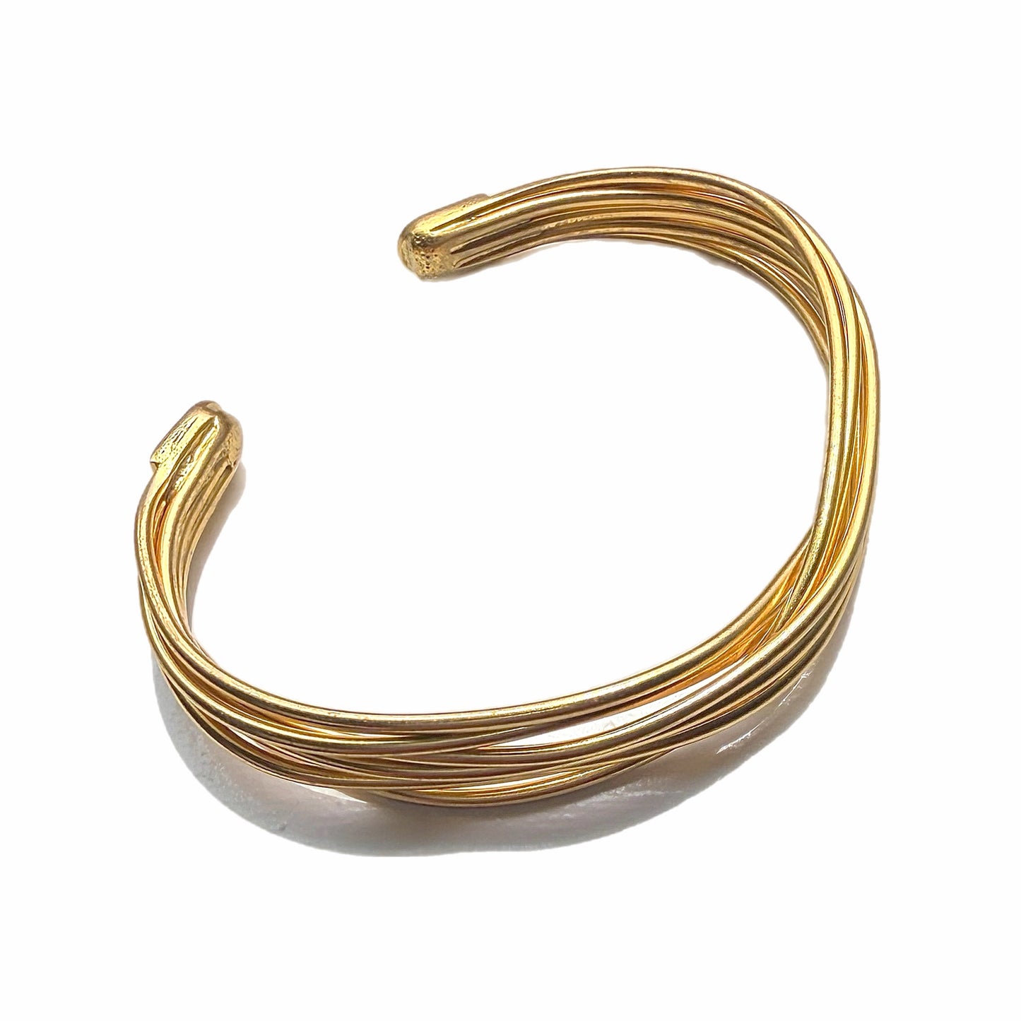 Gold-plated wire cuff bracelet on a marble surface with a white background 