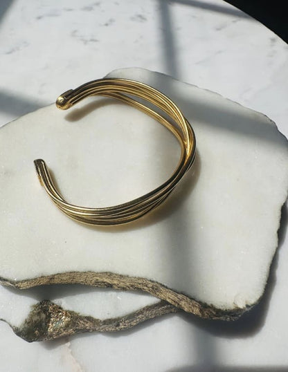 Gold-plated wire cuff bracelet on a marble surface with a natural wood piece