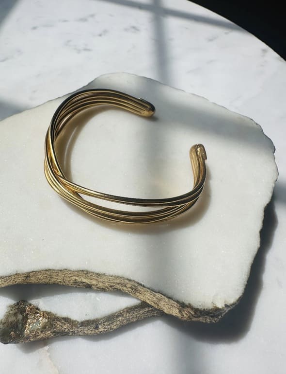 Side angle of Gold-plated wire bracelet on a white stone surface with a natural branch
