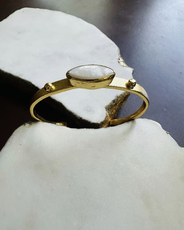 Gold-plated bangle with mother of pearl center  propped horizontally on a white stone surface