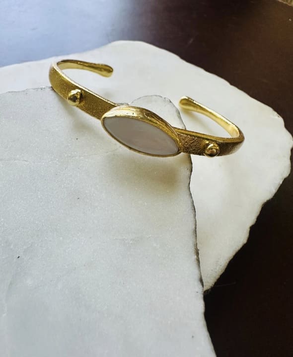 Gold-plated dainty bangle with miter of pearl white stone center placed on white marble slab