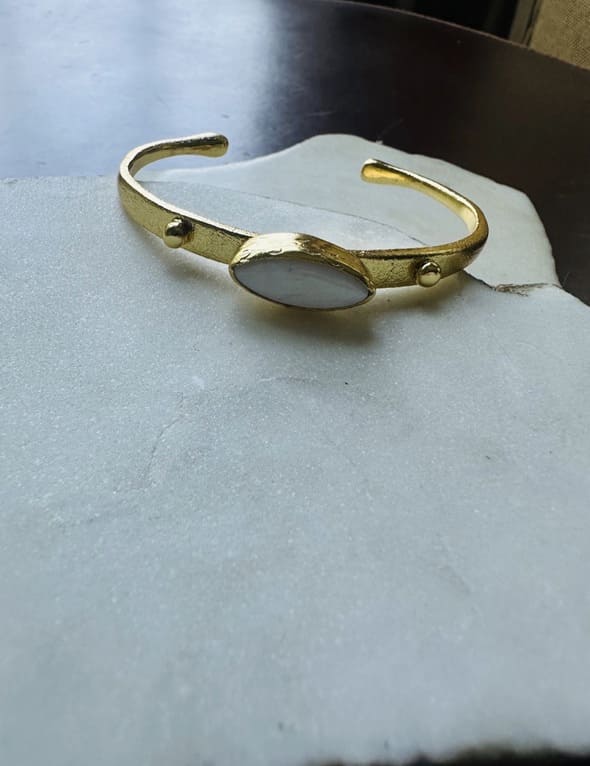 Gold-plated dainty bracelet with mother of pearl center laying on a white marble surface