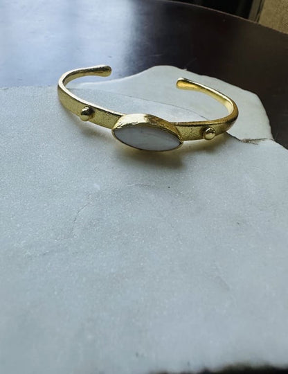 Gold-plated dainty bracelet with mother of pearl center laying on a white marble surface