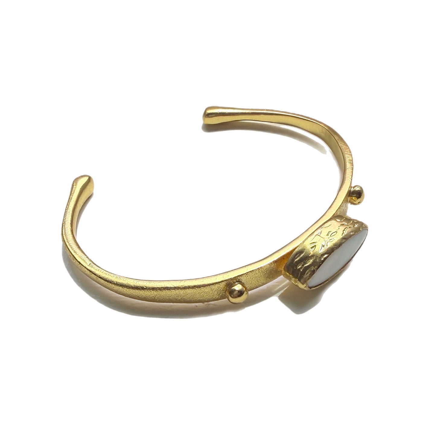 Gold-plated dainty bracelet with mother of pearl center laying on a white background Facing right 