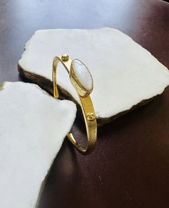 Gold-plated mother of pearl bangle propped up on stone on a textured surface