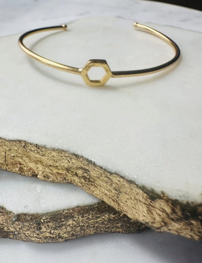 Gold bracelet with a hexagonal charm on a marble surface