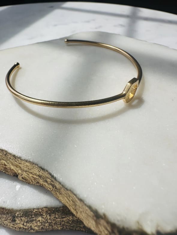 Gold-played dainty stackable bangle on a white surface with a natural wood edge.