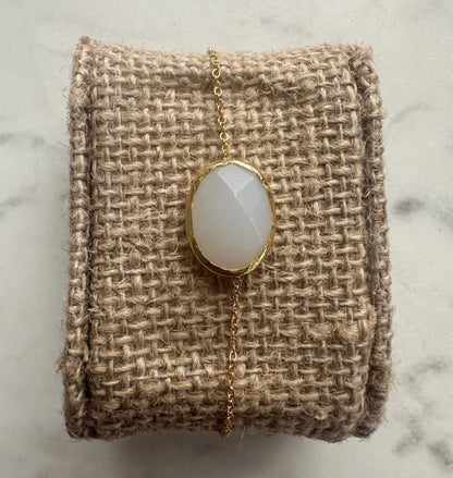 Minimal handmade gold-played chain bracelet with a snow Quartz pendant on a textured beige fabric against a marble background