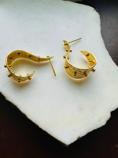 Gold modern hoop earrings on a white stone surface