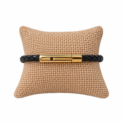 Thin black leather braided bracelet with gold buckle on jute jewelry pillow 