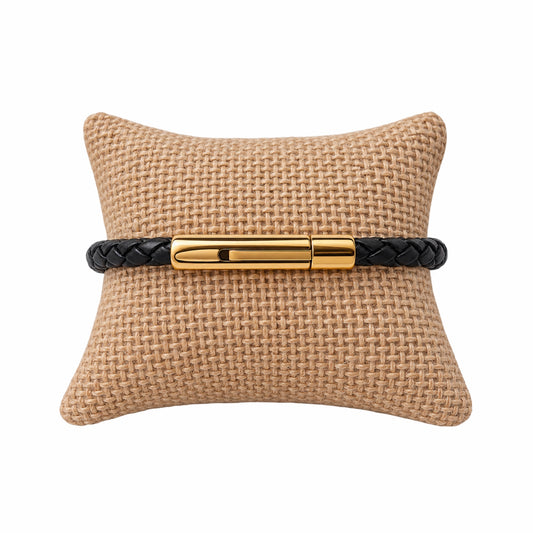 Thin black leather braided bracelet with gold buckle on jute jewelry pillow 