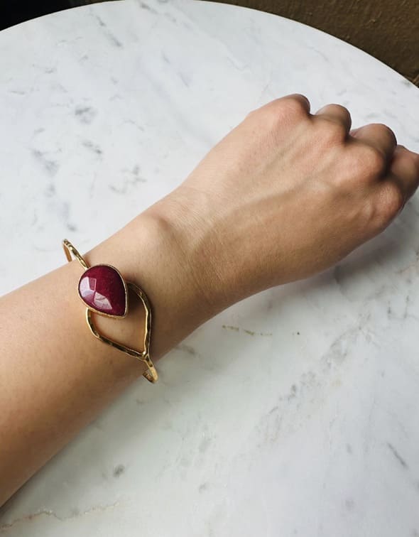 Artisanal Gold bracelet with a red ruby gemstone on a wrist on marble surface