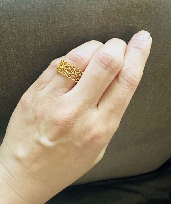 Gold-plated lace ring on a finger against a brown background