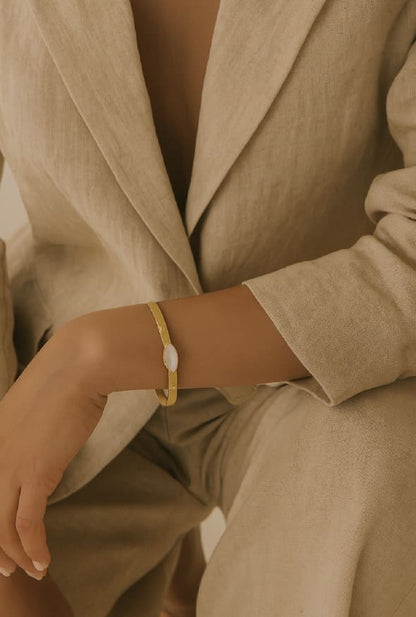 Woman wearing a beige pantsuit and handmade gold-plated mother of pearl bracelet with a blurred background
