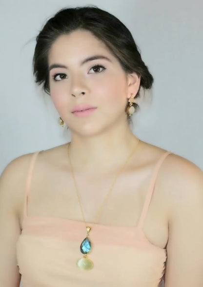 Woman wearing a beautiful long gold-plated necklace with a snow Quartz and labradorite pendant against a plain background