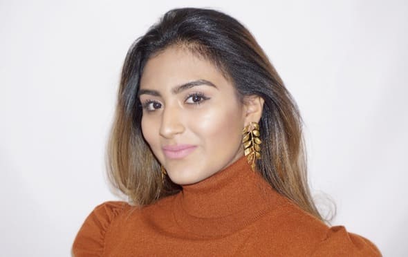 Woman wearing a brown turtleneck sweater and artisanal gold-plated vine leaf earrings with a plain background
