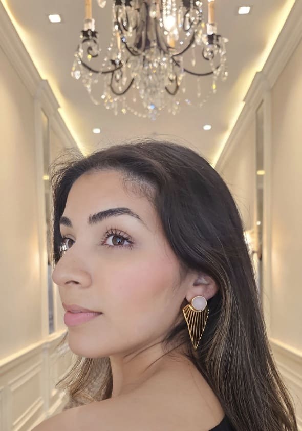 Woman looking over her shoulder wearing handmade gold-plated rose quartz earrings in a luxurious interior setting with a chandelier