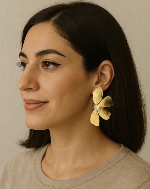 Woman wearing handmade sustainable gold-plated contemporary flower-shaped earrings with pearl against a neutral background
