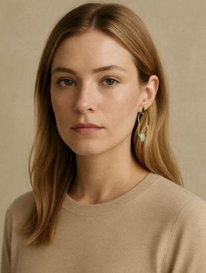 Woman wearing handmade sustainable gold-plated hoop earrings with a beige background