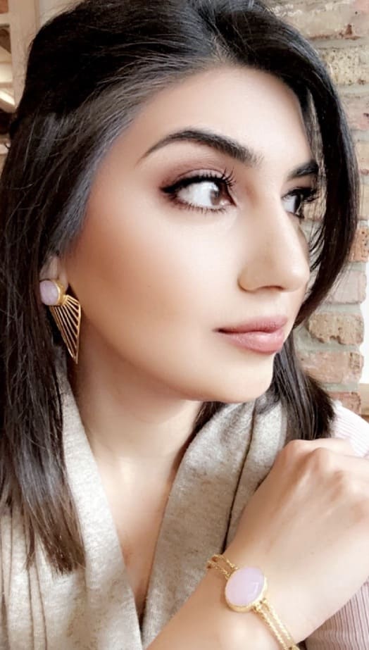 Woman wearing artisanal sustainable gold-plated rose quartz earrings and bracelet against a brick wall background