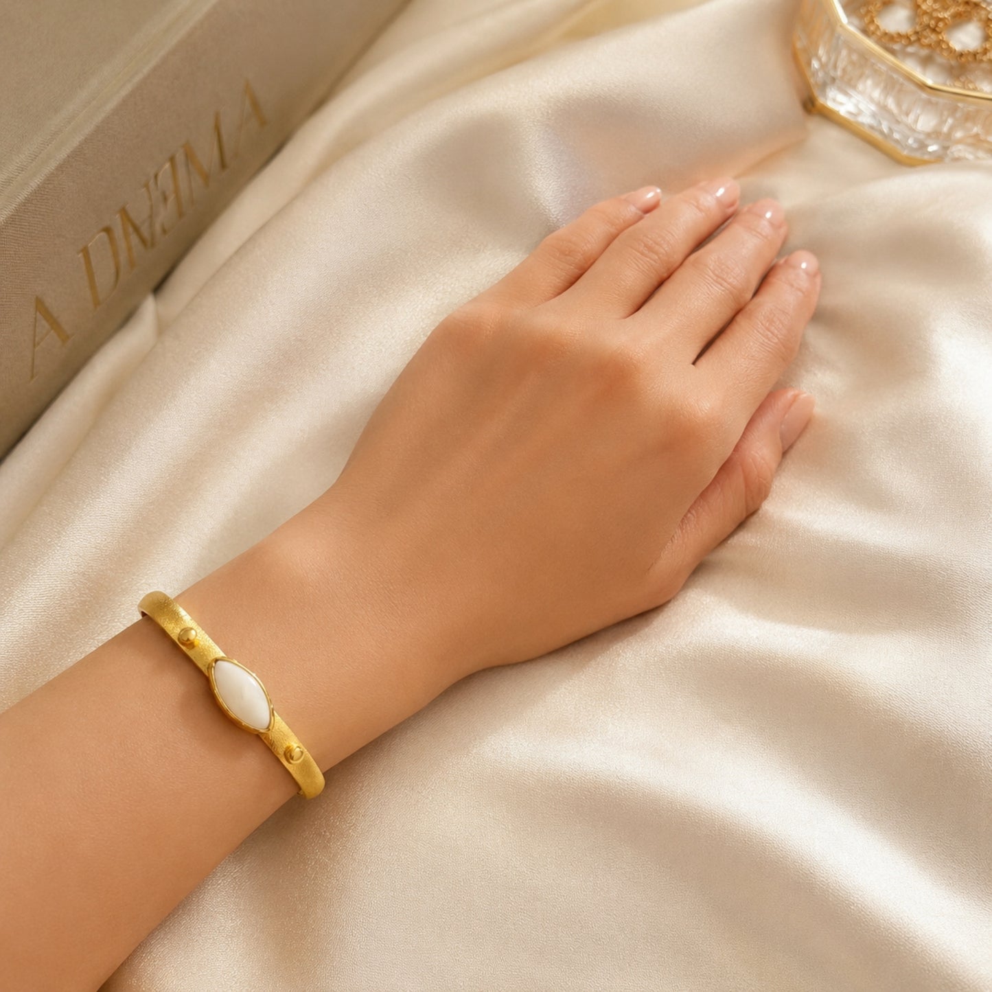 Woman wearing a handmade gold-plated mother of pearl bracelet with a satin background