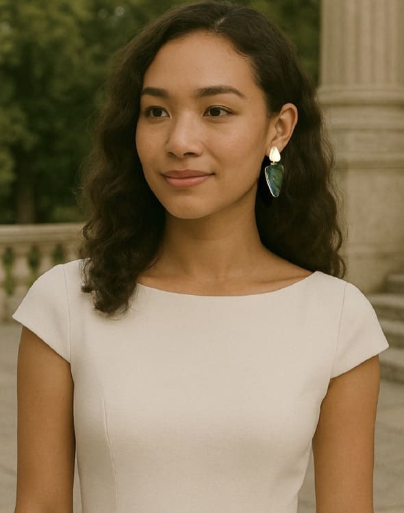 Woman wearing a light-colored dress and handmade eco-friendly contemporary snow Quartz and multi-colored stone statement earrings with a blurred outdoor background 