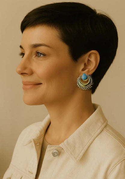Woman with short hair wearing stylish beige jean jacket and handmade bold gold-plated turquoise stud earrings against neutral background 