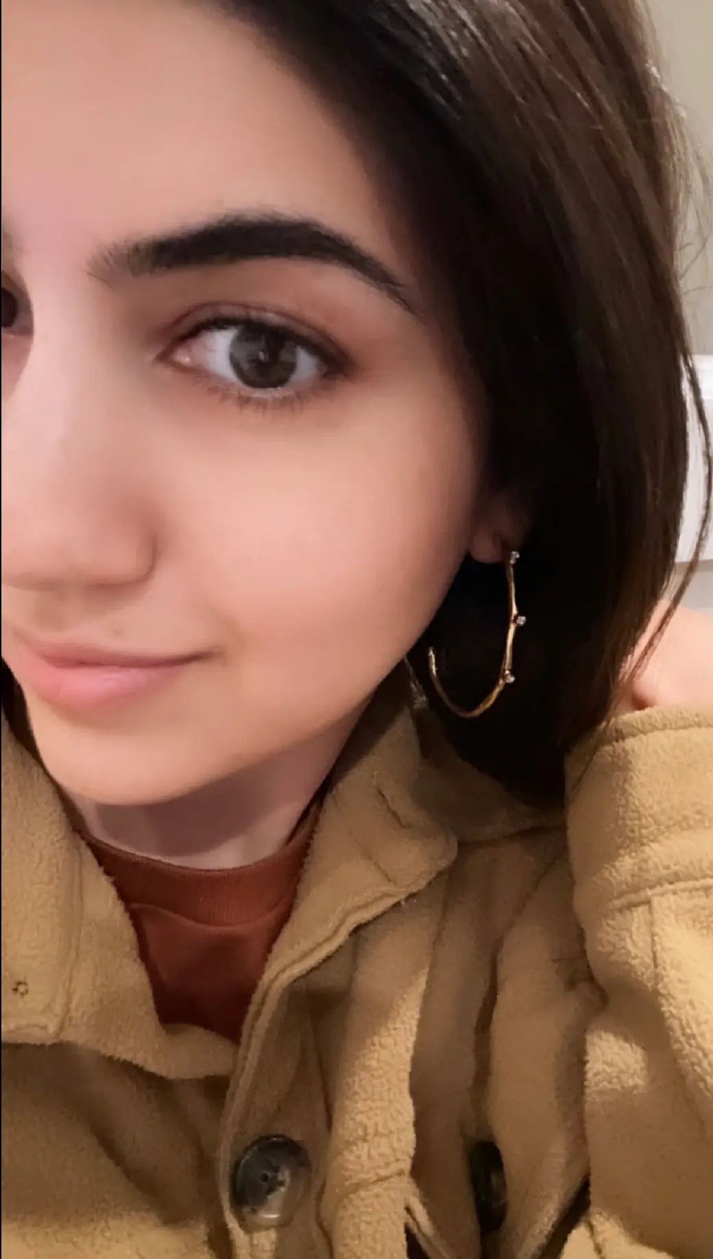 Woman wearing fleece and gold-plated modern cz elongated hoop earrings 