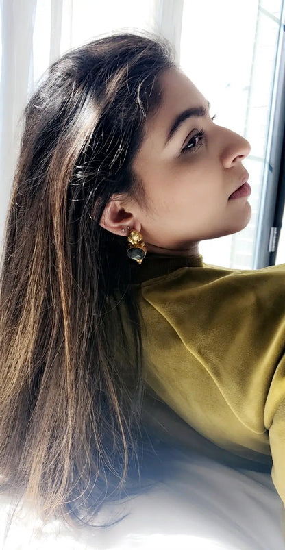 Woman wearing gold-played labradorite Fleur-de-lis earrings with a blurred background