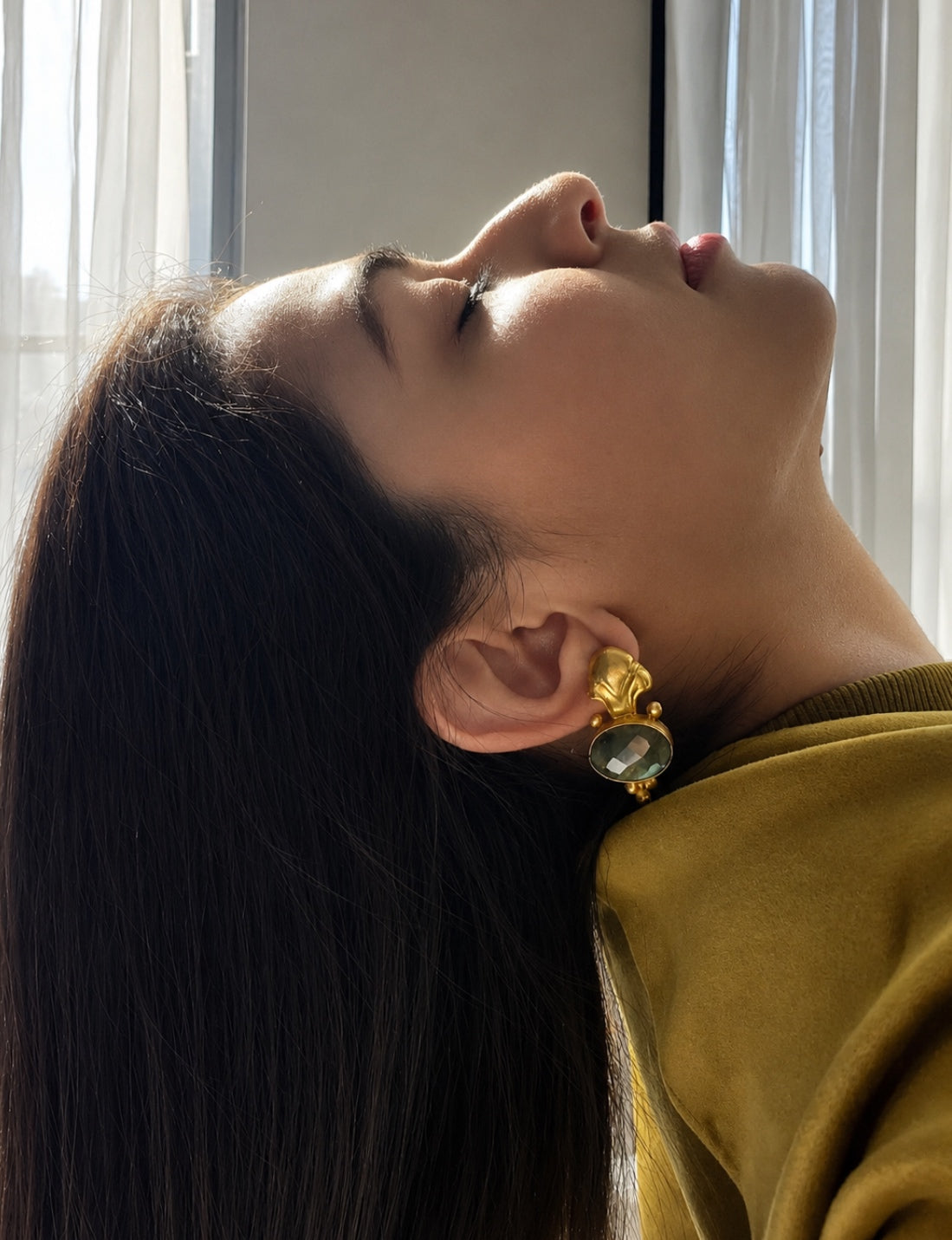 Woman wearing green top and beautiful gold-plated Fleur-de-Lis labradorite earrings with a blurred background