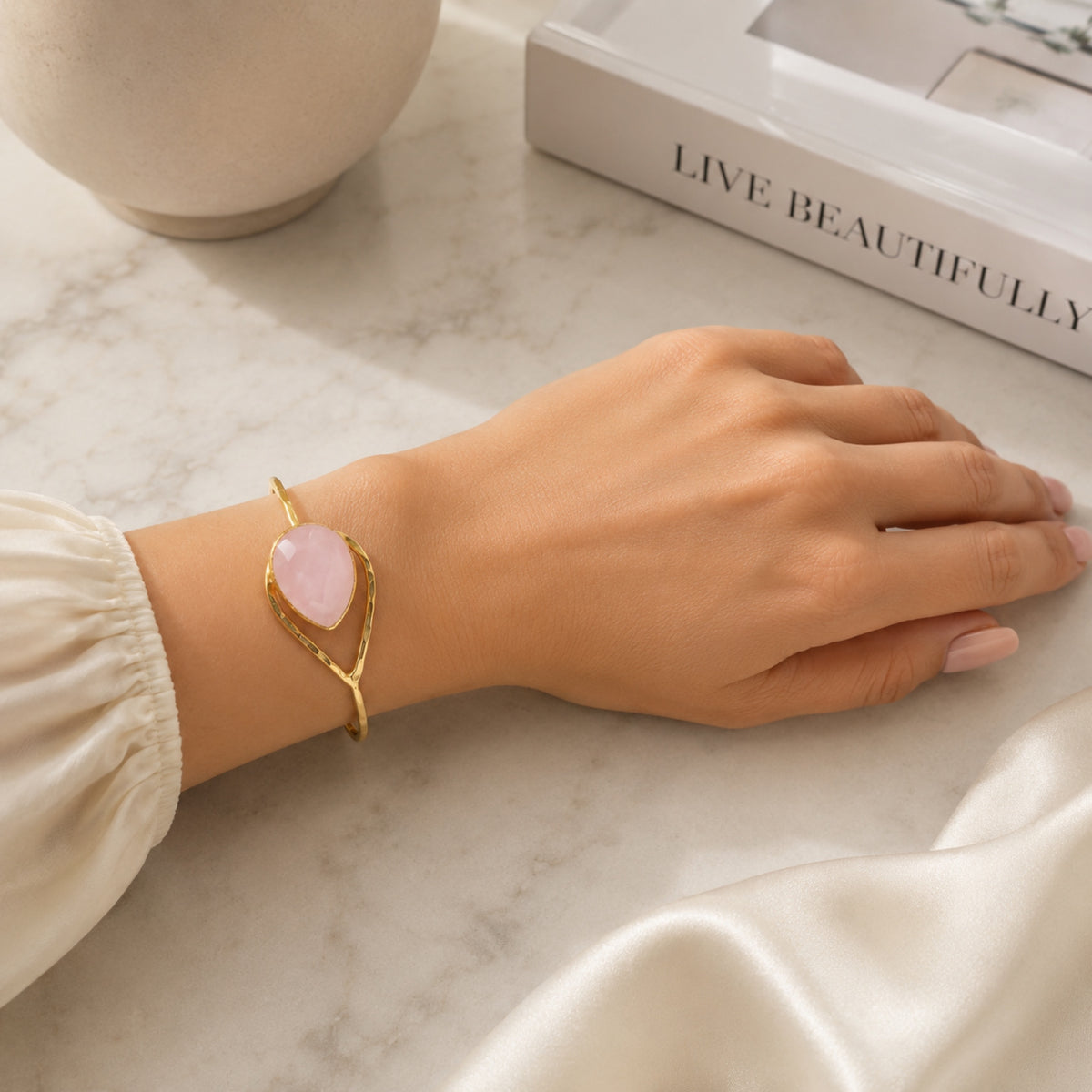 Handmade gold-plated rose quartz gemstone bangle on arm over white marble