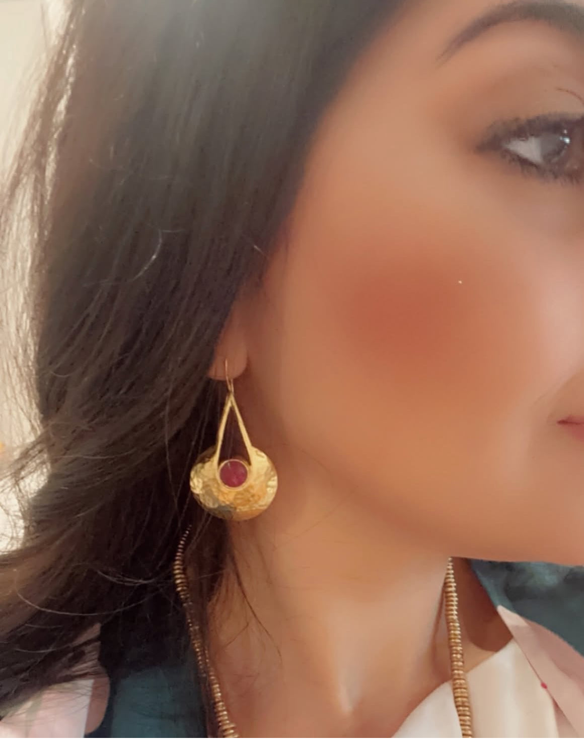A close-up image of a woman wearing gold high end gold-plated ruby earrings and lulusar outfit 