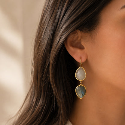 Woman wearing a white collared shirt with artisanal sustainable gold-plated teardrop labradorite and snow Quartz dangle earrings against beige backdrop