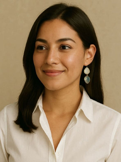 Woman wearing a white collared shirt with artisanal sustainable gold-plated teardrop labradorite and snow Quartz dangle earrings against beige backdrop