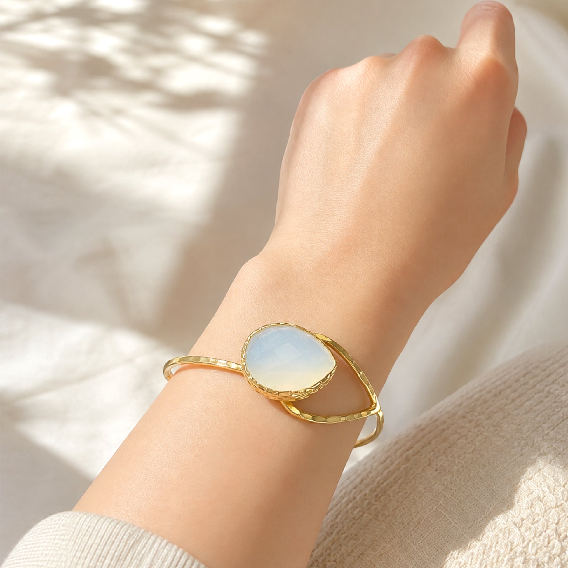 Gold-plated artisanal bracelet with a teardrop snow Quartz stone on a wrist against a white background with shadows 