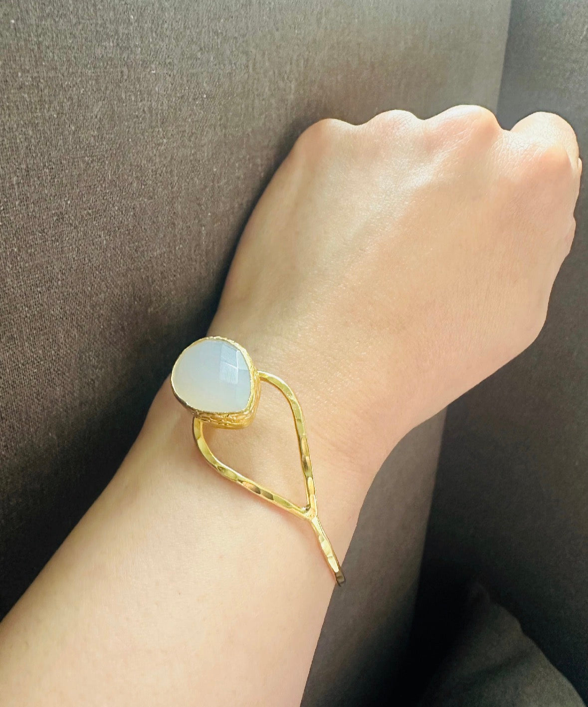 Wrist wearing Gold-plated bracelet with a teardrop snow Quartz stone against a dark background