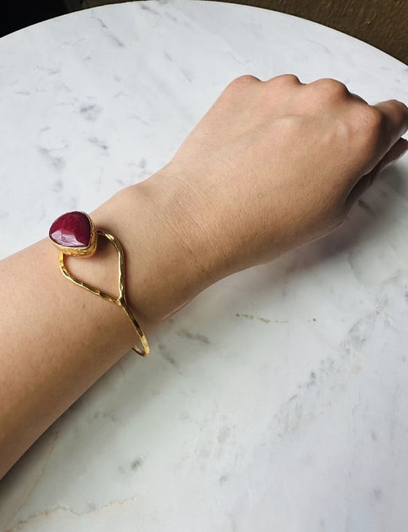 Gold-plated artisanal bracelet with a red ruby gemstone on a wrist against marble surface