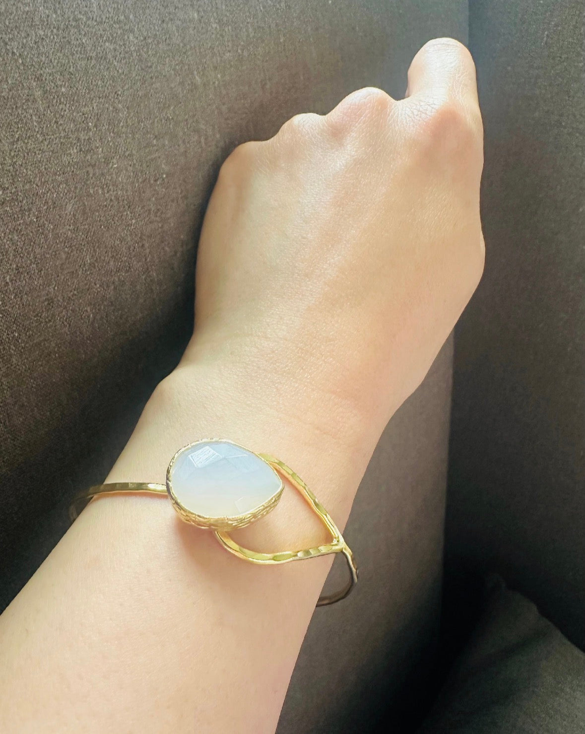 Gold-plated artisanal bracelet with a teardrop snow Quartz stone on a wrist against a dark background
