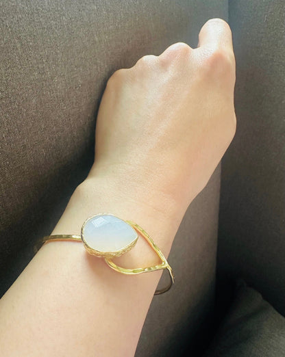 Gold-plated artisanal bracelet with a teardrop snow Quartz stone on a wrist against a dark background