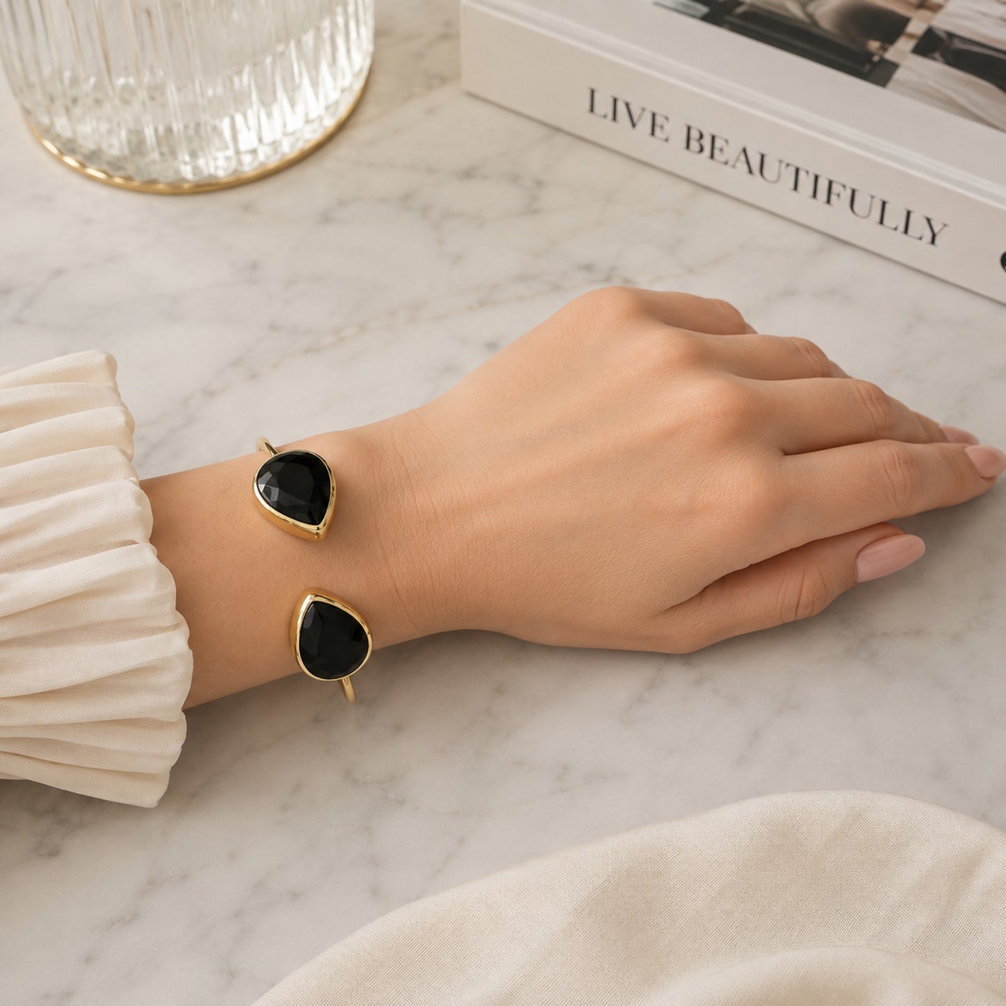 Hand wearing gold-plated sustainable cuff bangle with two teardrop onyx stones against a white surface