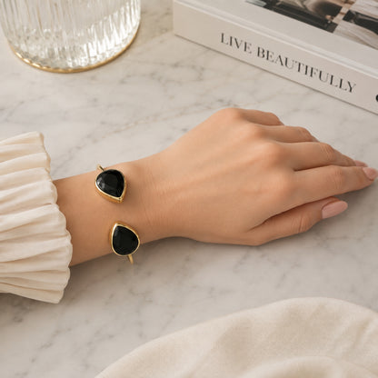 Hand wearing gold-plated sustainable cuff bangle with two teardrop onyx stones against a white surface