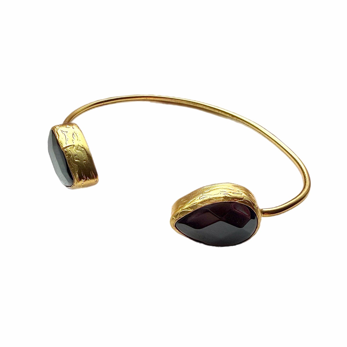 Gold-plated cuff bracelet with two onyx black stones on a white stone surface facing left