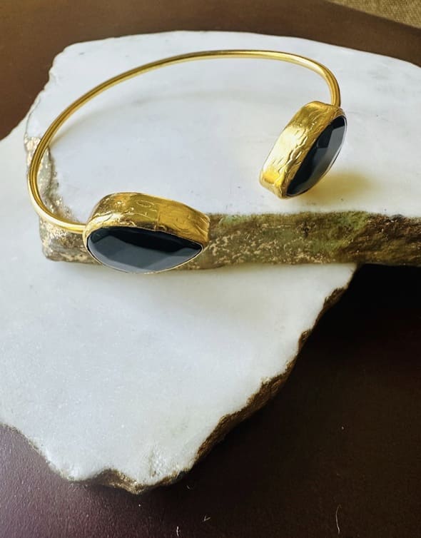 Gold-played cuff bracelet with two onyx black stones on a white stone surface