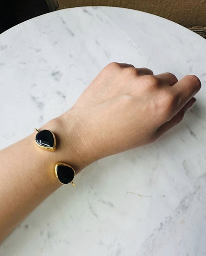 Hand wearing gold-played sustainable cuff bangle with two teardrop onyx stones against a marble surface