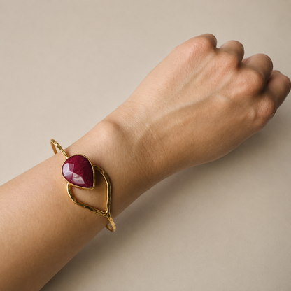 Arm with Artisanal Gold-plated hammer-finished bracelet with a red ruby gemstone on a white surface