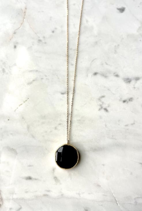 Zoomed-out image of artisanal sustainable gold-plated round onyx pendant necklace with long on a marble surface