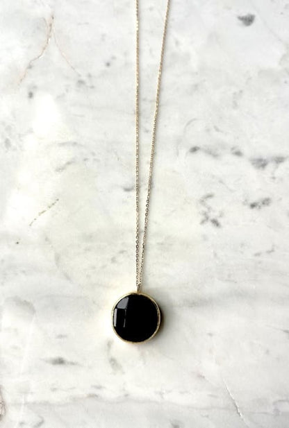 Zoomed-out image of artisanal sustainable gold-plated round onyx pendant necklace with long on a marble surface